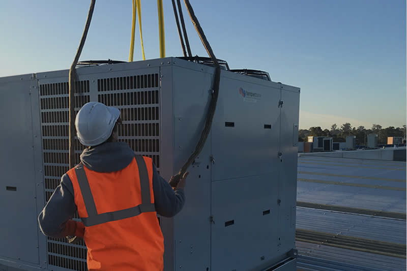 Technician guiding a rooftop package unit installation at a Melbourne commercial site